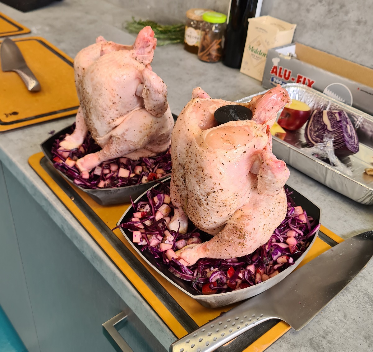 Připravená kuřata před grilováním na stojanu na drůbež Weber Deluxe Připravená celá dvě kuřata na stojanech na drůbež Weber Deluxe s červeným zelím v miskách